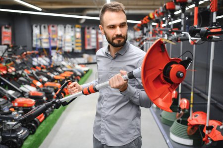customer with electric lawn trimmer in hands at garden equipment store.