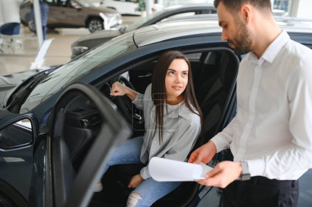 Zufriedene glückliche kaukasische Kundin sitzt am Steuer eines neuen Autos männliche Verkäuferin hilft ihr, es zu wählen.