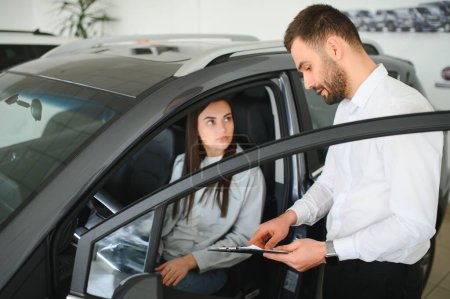 Zufriedene glückliche kaukasische Kundin sitzt am Steuer eines neuen Autos männliche Verkäuferin hilft ihr, es zu wählen.
