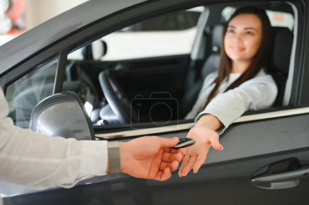 Distribuidor dando la llave al conductor femenino alegre mientras que vende el vehículo rojo moderno en concesionario.