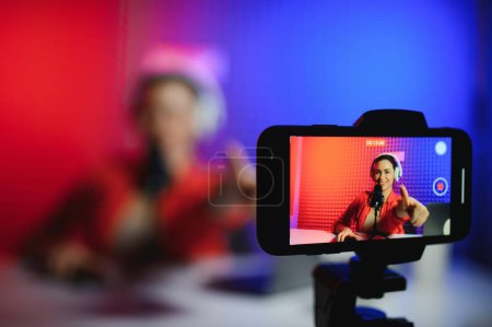 Positive trendige Bloggerin spricht vor Smartphone-Webcam auf Stativ, Aufnahmepost für Vlog.