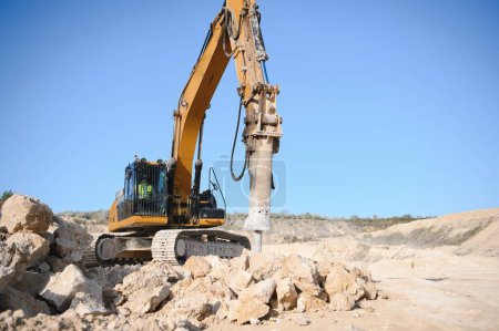 Marteau brise-roches hydraulique dans une carrière pour l'extraction de calcaire avec une excavatrice.