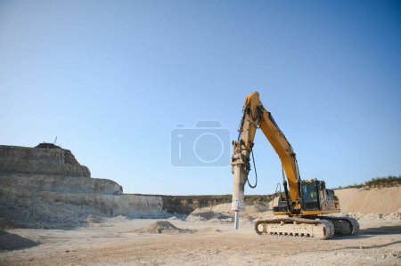 heavy organge excavator with shovel standing on hill with rocks.