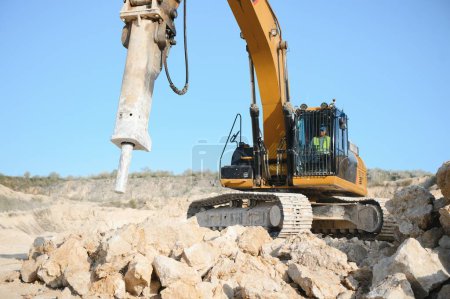 Hydraulic breaker hammer in a quarry for limestone mining with an excavator.