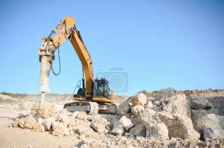 Hydraulic breaker hammer in a quarry for limestone mining with an excavator.