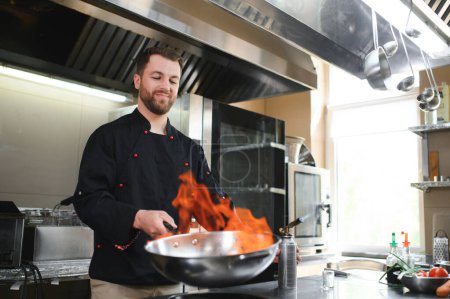Chef cooking and doing flambe on food in restaurant kitchen.