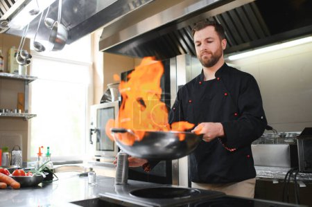 Chef cooking and doing flambe on food in restaurant kitchen.