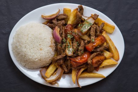Teller voll mit typisch peruanischem Lomo-Saltado-Rezept, begleitet von Reis, Paprika und roten Zwiebeln und hausgemachten Chips