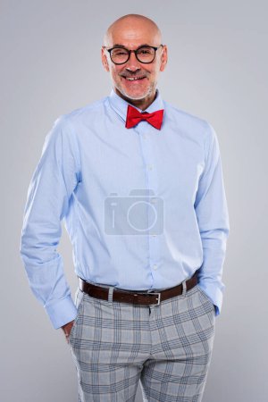 Photo for Shot of confident man standing at isolated grey background. Smiling caucasian male wearing bow tie and eyewear. Copy space. - Royalty Free Image