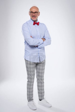 Photo for Full length of confident man standing with arms crossed at isolated white background. Smiling caucasian male wearing bow tie and checked trousers. Copy space. - Royalty Free Image