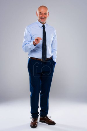 Téléchargez les photos : Pleine longueur de PDG masculin confiant debout sur fond gris. Le manager mature porte chemise et cravate. Il sourit dans un contexte isolé. Un cadre heureux vous pointant du doigt. - en image libre de droit