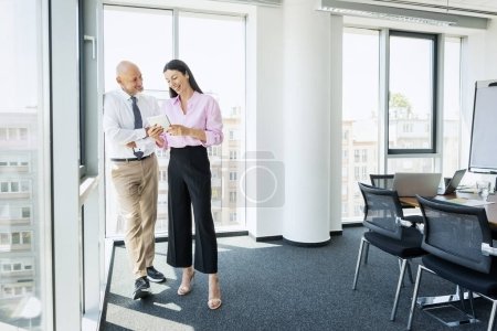 Photo for Full length of business people standing together at the office and using digital tablet. Attractive businesswoman and middle aged businessman looking at touchpad and discussing. - Royalty Free Image
