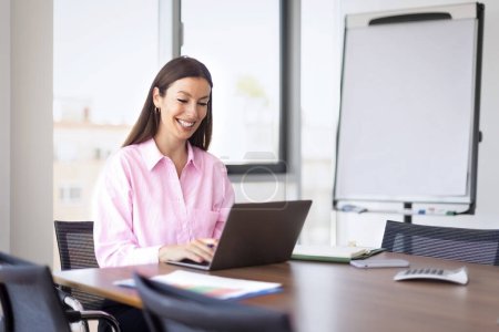 Foto de Smiling businesswoman sitting behind her laptop at office desk and working. - Imagen libre de derechos