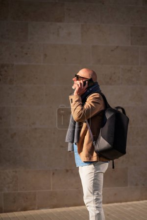 Photo for Mature businessman using mobile phone in the city. Man in casual clothes walking outdoors by a building. - Royalty Free Image