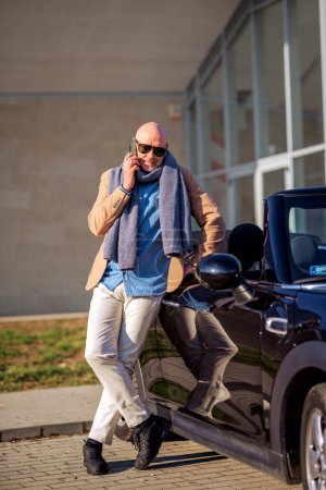 Photo for Full length of middle aged man wearing casual clothes and using mobile phone while standing outdor beside his car. - Royalty Free Image