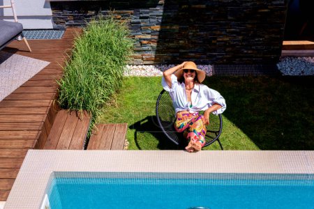 Téléchargez les photos : High angle shot of an attractive woman wearing straw hat and beachwear while relaxing at the pool. - en image libre de droit