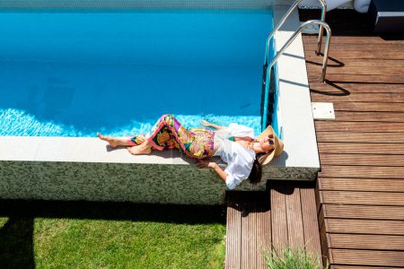 Téléchargez les photos : Full length of an attractive woman wearing white shirt and sun hat while relaxing by the poolside. Copy space. - en image libre de droit