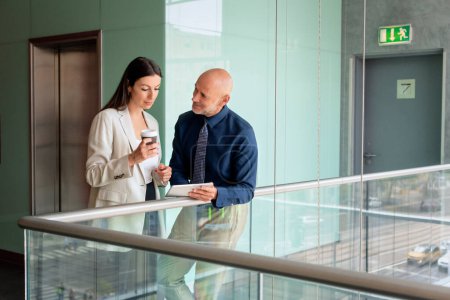 Photo for Shot of businesswoman and businessman standing in a modern office together. Professional woman drinking coffee while businessman holding touchpad in his hand. Teamwork. - Royalty Free Image