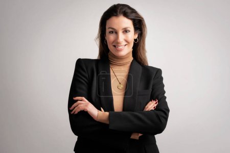 Foto de Close-up of an attractive mid aged woman smiling and looking at camera. Brunette haired female wearing black blazer and standing at isolated background. Copy space. - Imagen libre de derechos