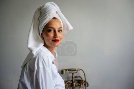 Foto de Portrait of gorgeous young woman wearing white shirt and turban towel on head while relaxing in the bathroom. - Imagen libre de derechos
