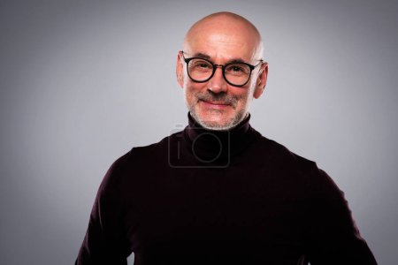 Photo for Headshot of confident man standing at isolated grey background. Smiling male wearing eyewear and turtleneck sweater. Copy space. - Royalty Free Image