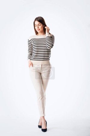 Photo for Full length of an attractive woman standing at isolated background. Confident young female is having brunette hair. She is in striped sweater against white background. Copy space. - Royalty Free Image