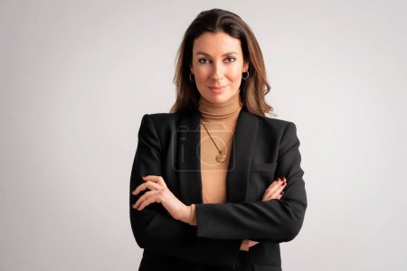 Studio portrait of an attractive woman toothy smiling and looking at camera. Brunette haired female wearing blazer and standing against isolated white background. Copy space. 