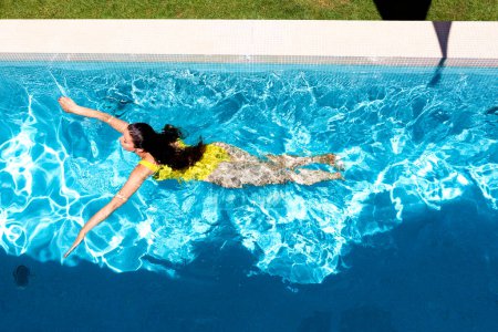 Photo for High angle shot of a woman wearing yellow swimsuit and swimming in the swimming pool. - Royalty Free Image