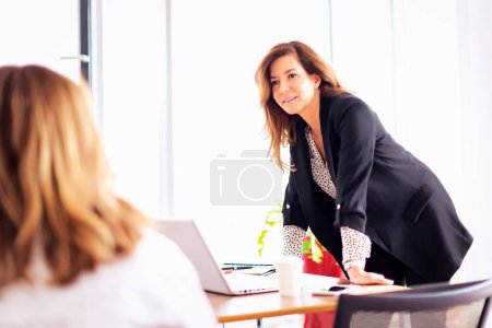 Téléchargez les photos : Groupe de femmes d'affaires utilisant un ordinateur portable tout en se tenant au bureau et de présenter son idée sur la réunion d'affaires. Travail d'équipe dans un bureau moderne. - en image libre de droit