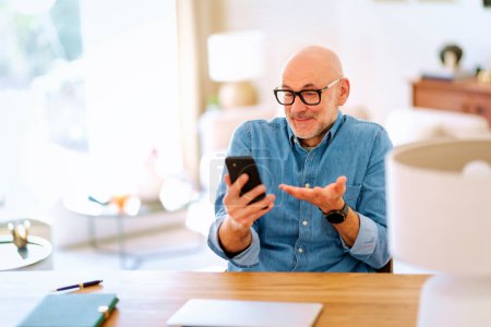 Photo for Surprised man wearing casual clothes and text messaging while sitting in his modern home. - Royalty Free Image