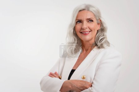 Téléchargez les photos : Portrait en studio d'une femme âgée aux cheveux gris regardant la caméra et souriant tout en se tenant debout sur un fond blanc isolé. Espace de copie. - en image libre de droit