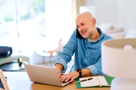 Photo for Confident senior man using notebook at home. Mid aged male working online and sitting at desk. Home office. - Royalty Free Image