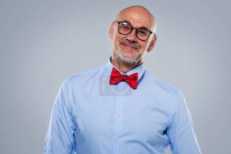 Foto de Retrato de estudio de un hombre de mediana edad con gafas y pajarita en un fondo gris aislado. Copiar espacio. - Imagen libre de derechos