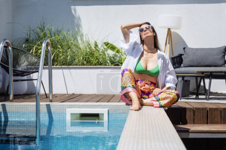 Téléchargez les photos : Portrait shot of attractive woman wearing sunglasses and beachwear while relaxing outdoor on a sunny day. - en image libre de droit