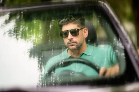 Foto de Un hombre guapo con gafas de sol y sentado en un coche convertible y conduciendo en la carretera. - Imagen libre de derechos