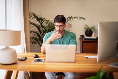Téléchargez les photos : Homme d'affaires d'âge moyen assis à un bureau et utilisant un ordinateur portable. Homme d'affaires ayant une conférence en ligne. Bureau à domicile. - en image libre de droit