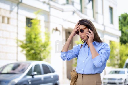 Photo for Worried woman with brown hair and eyewear standing on the street and having a call. Attractive business woman wearing casual clothes. - Royalty Free Image