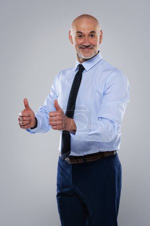 Téléchargez les photos : Prise de vue d'un homme d'affaires mature gesticulant les pouces levés et souriant. Homme confiant portant chemise et cravate. Espace de copie. - en image libre de droit