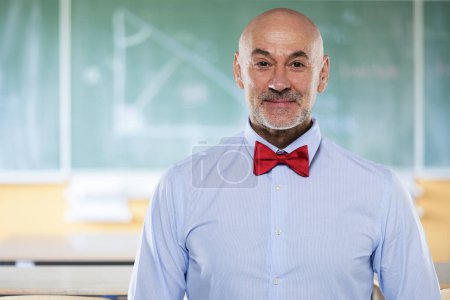 Photo for Portrait of mid aged male teacher standing in front of blackboard. Confident math professor wearing shirt and bow tie. - Royalty Free Image