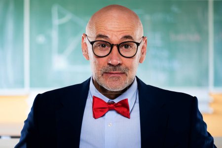 Foto de Profesor de matemáticas de mediana edad de pie frente a la pizarra en el aula. Hombre profesor buscando sorprendido. - Imagen libre de derechos
