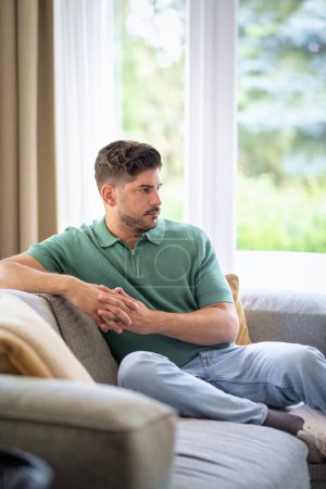 Téléchargez les photos : Portrait d'un homme confiant se relaxant sur le canapé à la maison. Homme d'âge moyen portant des vêtements décontractés. - en image libre de droit