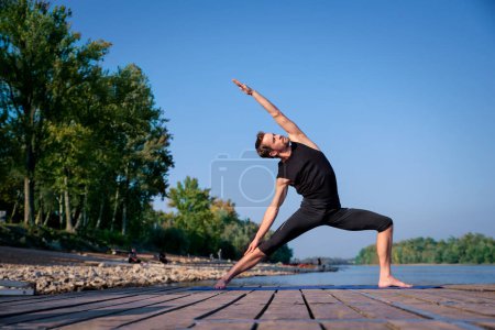 Foto de Longitud completa del hombre caucásico practicando yoga en el muelle junto al lago. - Imagen libre de derechos