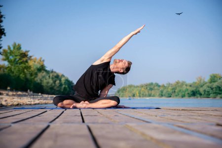 Téléchargez les photos : Toute la longueur de l'homme caucasien pratiquant le yoga sur jetée par lac. - en image libre de droit