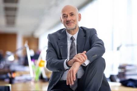 Photo for A middle-aged businessman is sitting in his office. Confident professional man wearing suit and tie. - Royalty Free Image