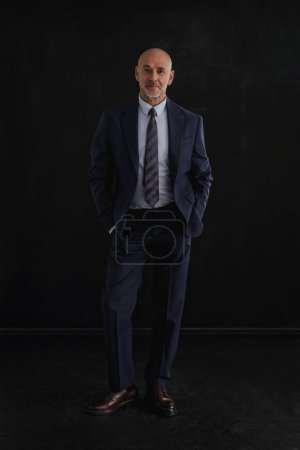 Photo for Mid aged man studio portrait at black background. A bald and stubbled man wearing suit at isolated background. Full length shot. Copy space. - Royalty Free Image