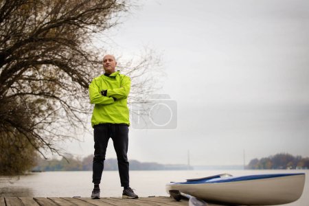 Photo for A middle-aged man standing on the jetty and ready to go kayaking. Active sporty man wearing dry suit. Full length shot. - Royalty Free Image