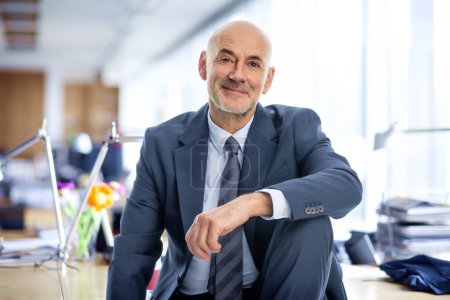 Foto de Un hombre de negocios de mediana edad está sentado en su oficina. Hombre profesional confiado que usa traje y corbata. - Imagen libre de derechos