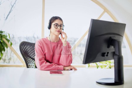 Foto de Asistente de servicio al cliente que usa auriculares mientras está sentada detrás de su computadora y trabaja en el centro de llamadas. - Imagen libre de derechos