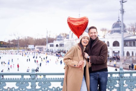 Photo for Couple standing together in city. They holding heart-shape ballon in ther hand and celebrating Valentines Day. Happy woman and handsome man celebrating their love - Royalty Free Image