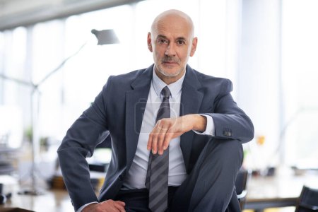 Foto de Un hombre de negocios de mediana edad está sentado en su oficina. Hombre profesional confiado que usa traje y corbata. - Imagen libre de derechos